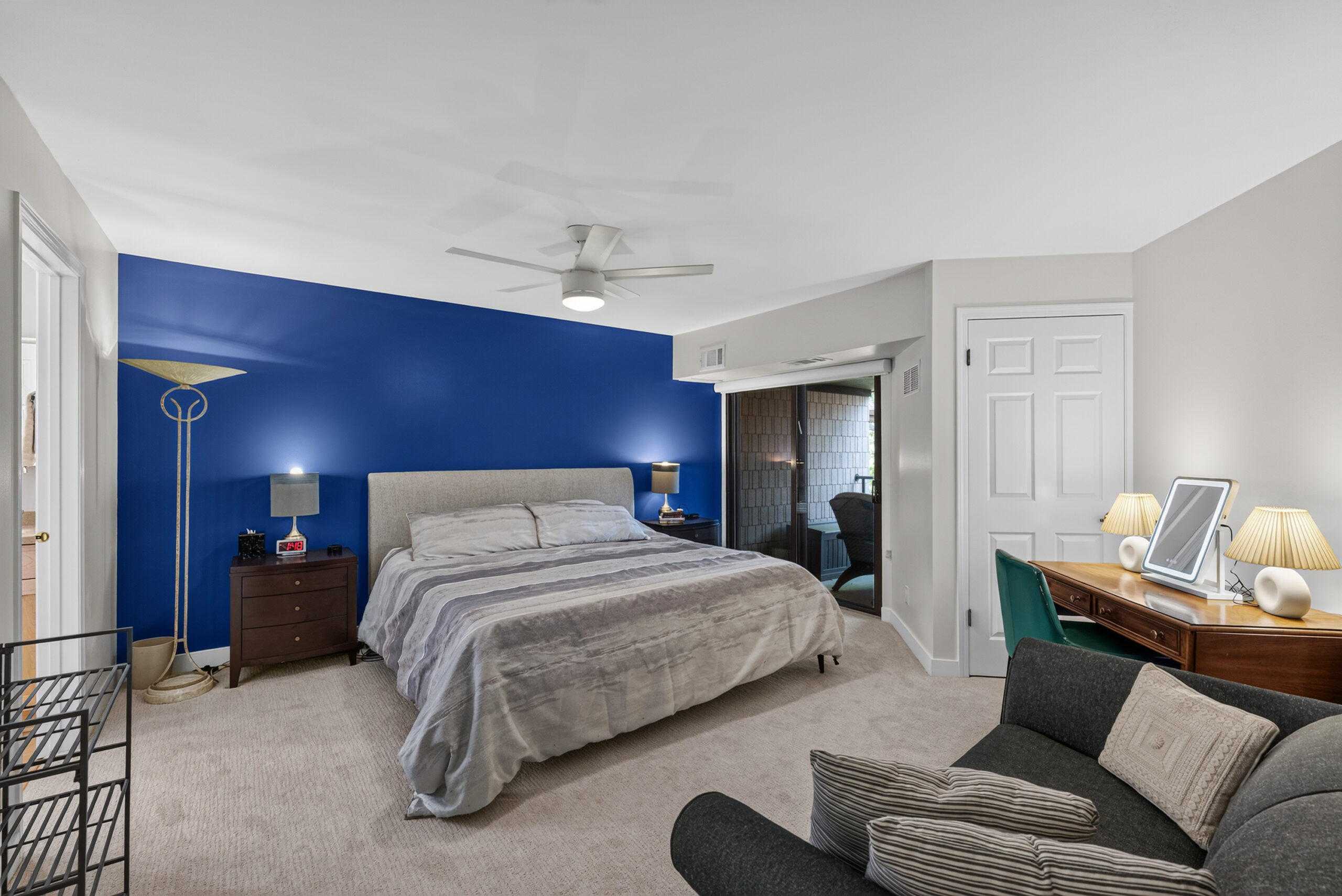 Bedroom with a blue accent wall behind a king bed, two nightstands, lamps, and a ceiling fan.