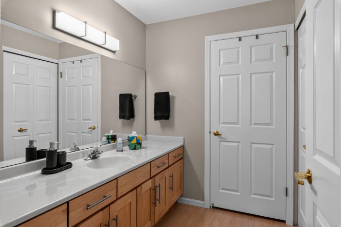 Wide shot of a modern bathroom with a double-sink vanity, wooden cabinets, and beige walls under bright overhead lighting.