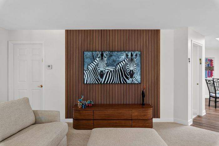 Living room with a zebra artwork mounted on a vertical wooden slat wall above a wooden console table. Beige sectional sofa in the foreground.