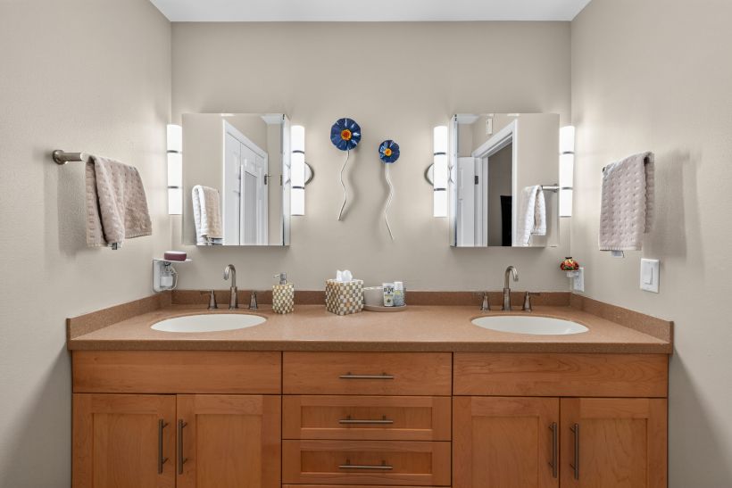 Double-sink bathroom vanity with wooden cabinets, beige countertop, and two mirrors with wall lights.