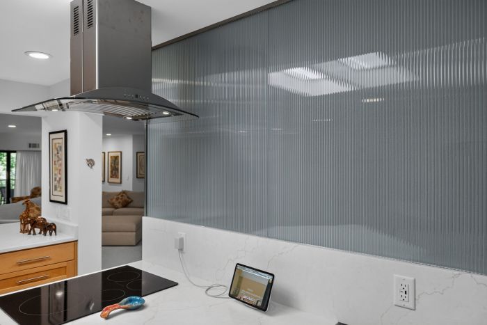 Modern kitchen with a curved stainless steel range hood over a glass induction cooktop and marble countertop.