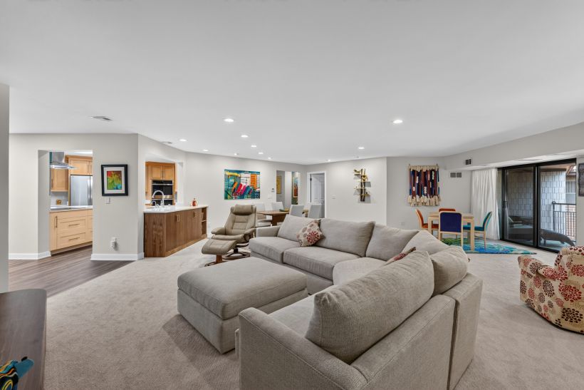 Open-concept living area with a large gray sectional, kitchen island, colorful wall art, and sliding glass doors to an outdoor space.