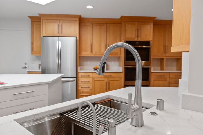 Modern kitchen with a stainless steel refrigerator and built-in oven, wooden cabinets, and a marble island sink in the foreground.