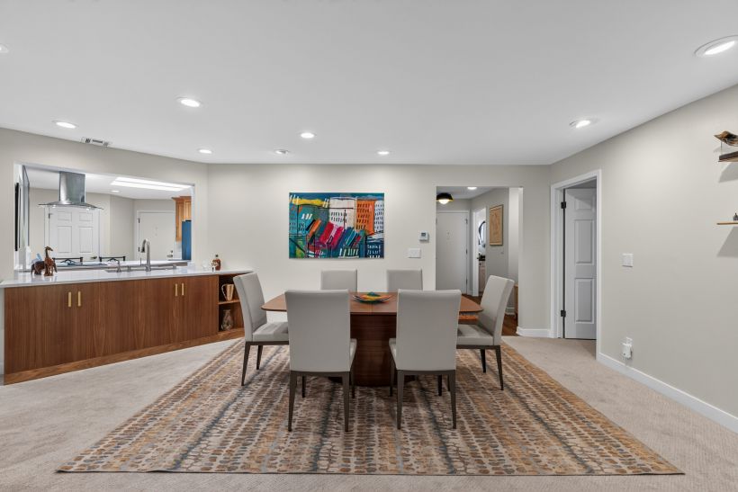 Open dining area with a wooden kitchen island, colorful abstract painting, and a rectangular table with gray chairs in a bright home.